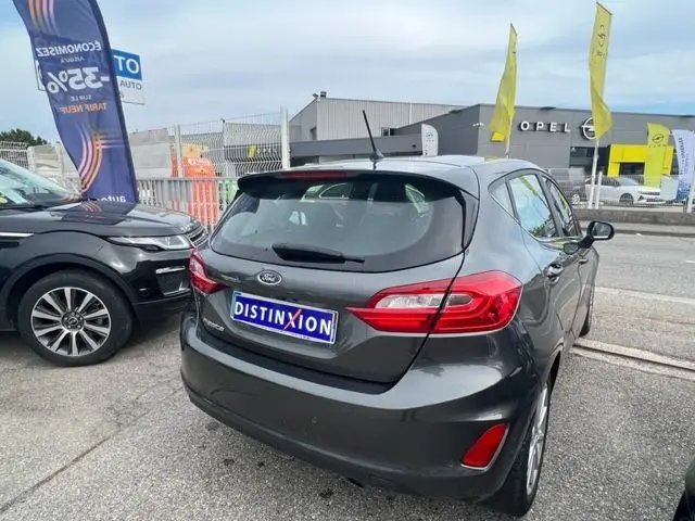 Vue 3/4 arrière droite d'une Ford Fiesta gris métallisé de 2018, avec feux arrière allongés et plaque Distinxion.
