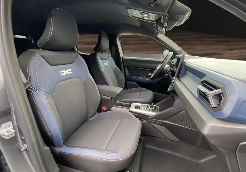 Vue intérieure côté conducteur du Dacia Duster 2025, sièges bi-matière gris et bleu avec logo distinctif sur appuie-tête.