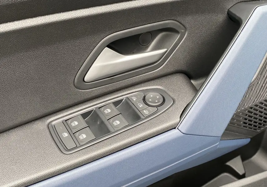 Détail de la porte avant gauche du Dacia Duster 2025 avec commandes de vitres et poignée argentée, garniture bleu et noire.