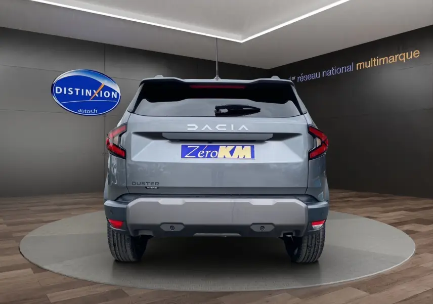 Vue arrière d'un Dacia Duster 2025 gris schiste avec logo DACIA en blanc et plaque "Zéro KM" dans un showroom.