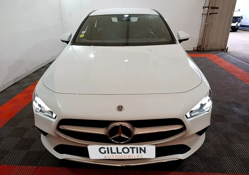 Vue avant d'une Mercedes CLA 200 d Business Line blanche avec phares LED allumés dans un garage.