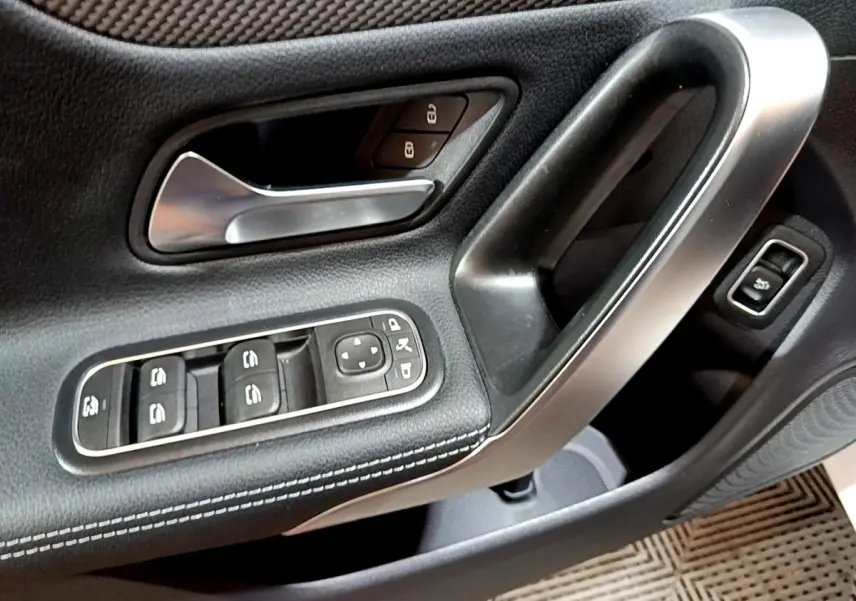 Gros plan sur la porte côté conducteur de la Mercedes CLA 200 d Business Line blanche, avec commandes électriques et poignée alu.
