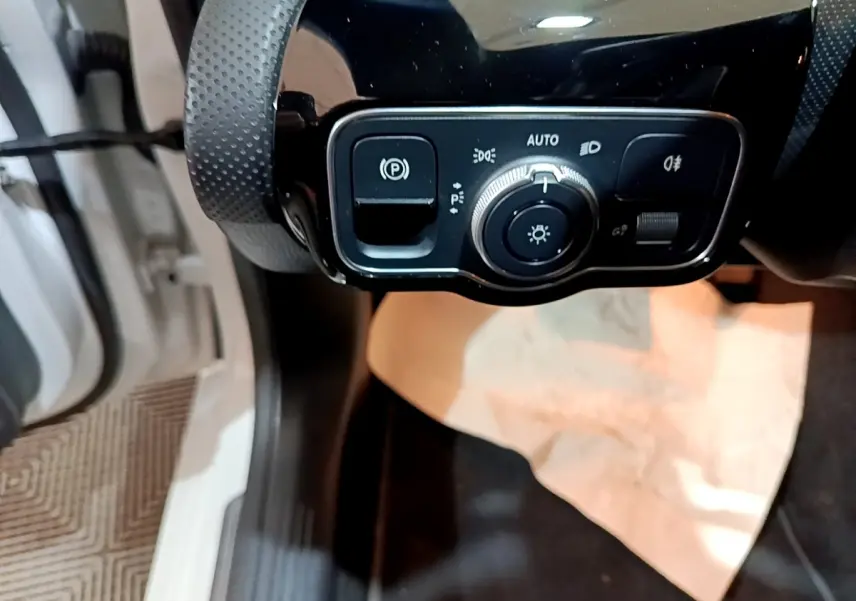 Gros plan sur le panneau de commande des phares et du frein à main électrique dans une Mercedes CLA 200 d Business Line blanche.