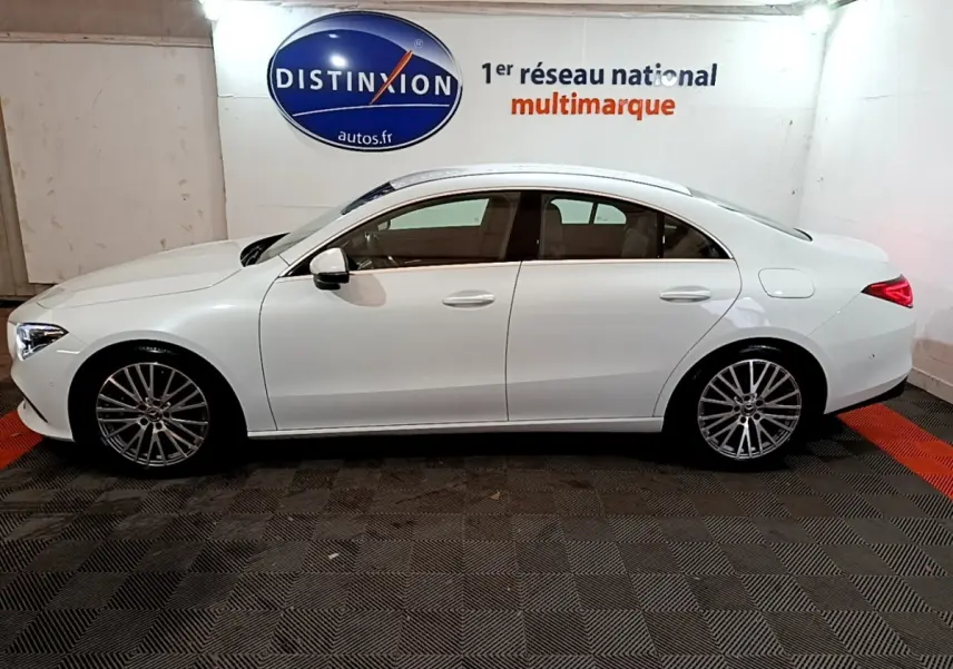 Vue de profil côté gauche d'une Mercedes CLA 200 d Business Line blanche, avec jantes alliage et feux arrière LED allumés.