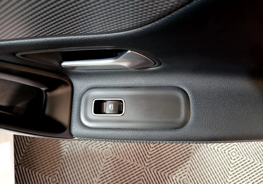 Détail du bouton de commande de la vitre électrique sur la porte intérieure côté conducteur d’une Mercedes CLA 200 d blanche.