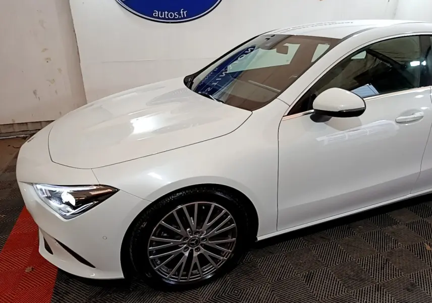 Vue 3/4 avant droit d'une Mercedes CLA 200 d Business Line blanche avec jantes alliage et phares LED allumés.