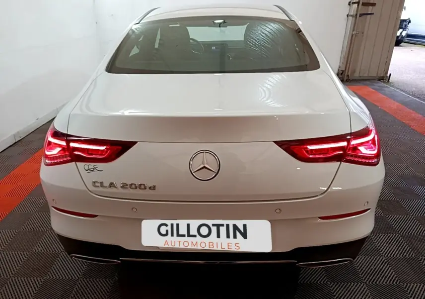 Vue arrière d'une Mercedes CLA 200 d Business Line blanche avec feux arrière LED allumés dans un garage.