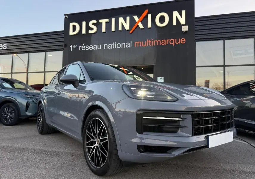 Vue 3/4 avant droite d’un Porsche Cayenne III Coupe 3.0 V6 S E-Hybrid 2024 en gris arctique avec jantes noires distinctives.