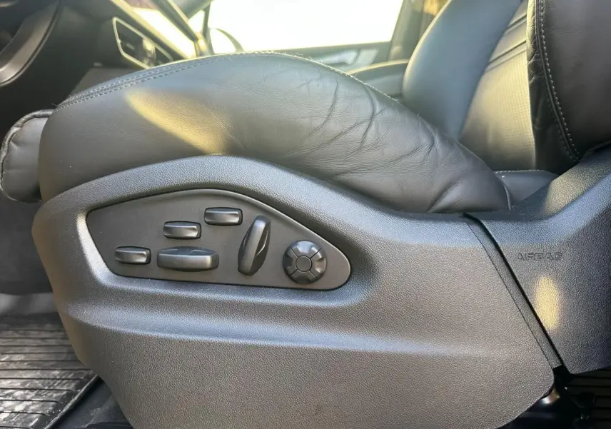 Gros plan sur les commandes électriques du siège conducteur en cuir noir du Porsche Cayenne Coupé gris arctique 2024.