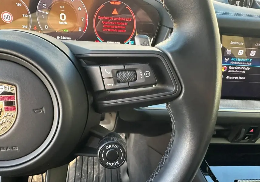 Vue rapprochée du volant noir du Porsche Cayenne 2024 avec commandes intégrées et affichage digital du tableau de bord.