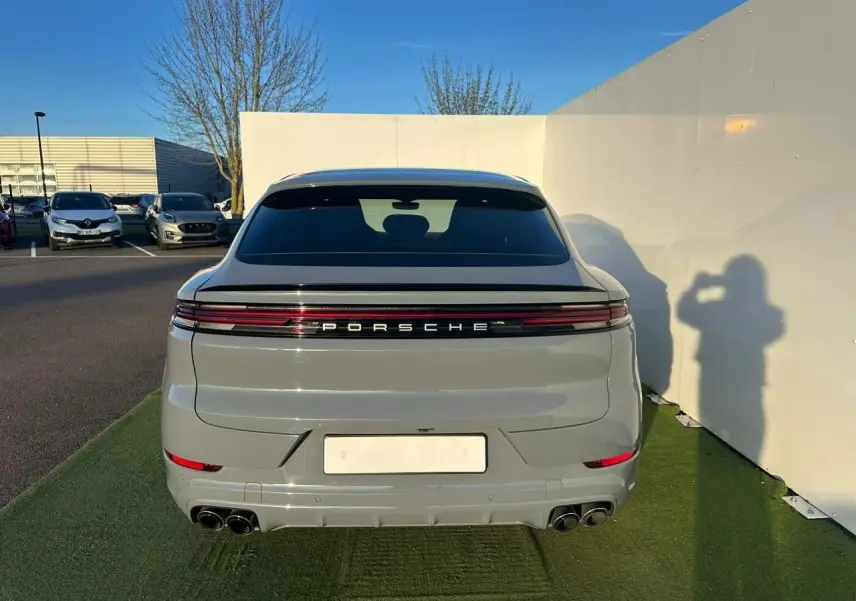 Vue arrière d'un Porsche Cayenne III Coupe 3.0 V6 S E-Hybrid 2024 en gris arctique avec feux LED continus et double sortie d'échappement.