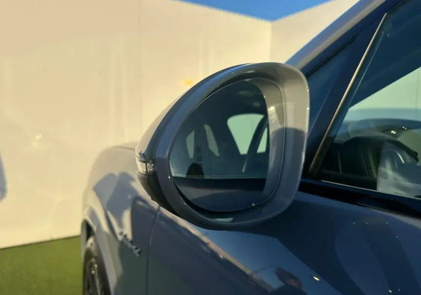Gros plan sur le rétroviseur côté gauche d’un Porsche Cayenne Coupe 2024 gris arctique, avec reflet de l’habitacle visible.