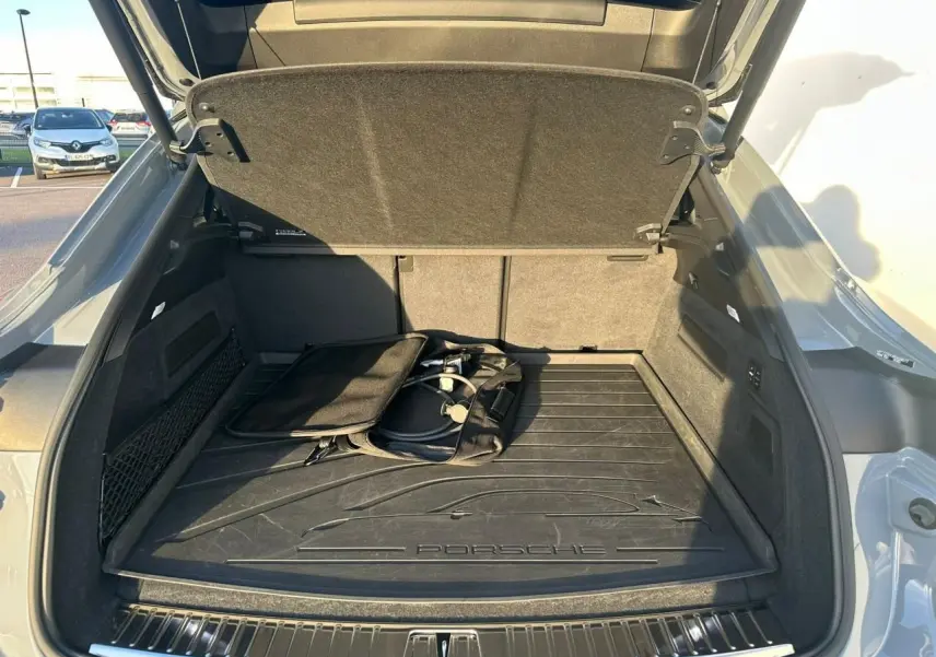 Coffre ouvert vu de l'arrière d'un Porsche Cayenne Coupé 2024 gris arctique avec tapis de coffre et câble de recharge hybride.