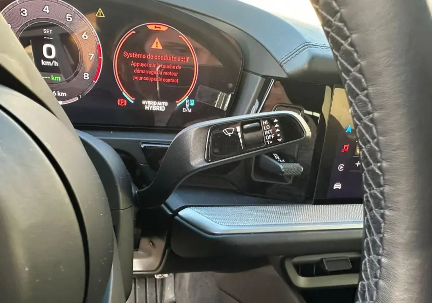 Vue rapprochée du tableau de bord et du volant d’un Porsche Cayenne hybride 2024 avec affichage numérique et commandes au volant.