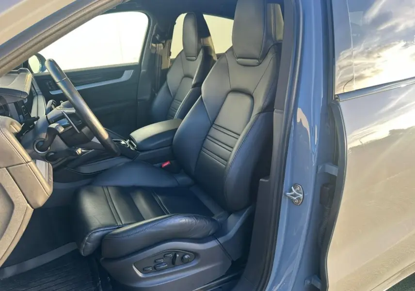 Vue intérieure côté conducteur du Porsche Cayenne 2024 gris arctique, mettant en valeur les sièges en cuir noir et le tableau de bord.
