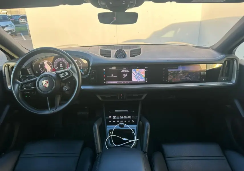 Vue intérieure frontale du tableau de bord du Porsche Cayenne 2024, avec écran tactile panoramique et volant multifonction noir.