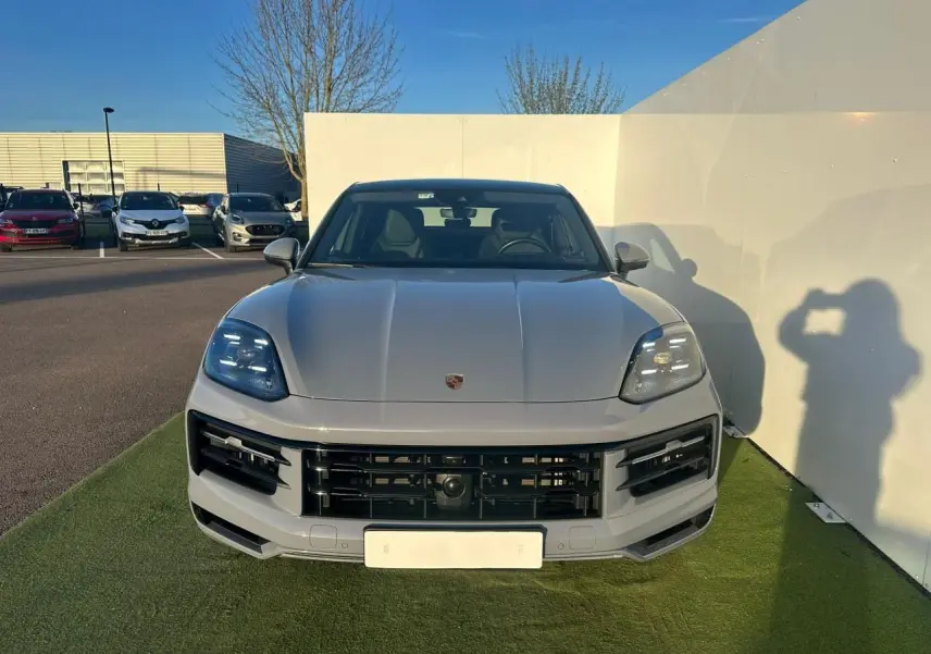 Vue avant d'un Porsche Cayenne III Coupe 3.0 V6 S E-Hybrid 2024 en gris arctique, avec calandre noire et phares LED.