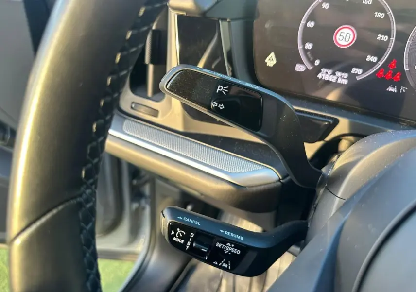 Gros plan sur les commandes au volant du Porsche Cayenne gris arctique, avec tableau de bord numérique en arrière-plan.