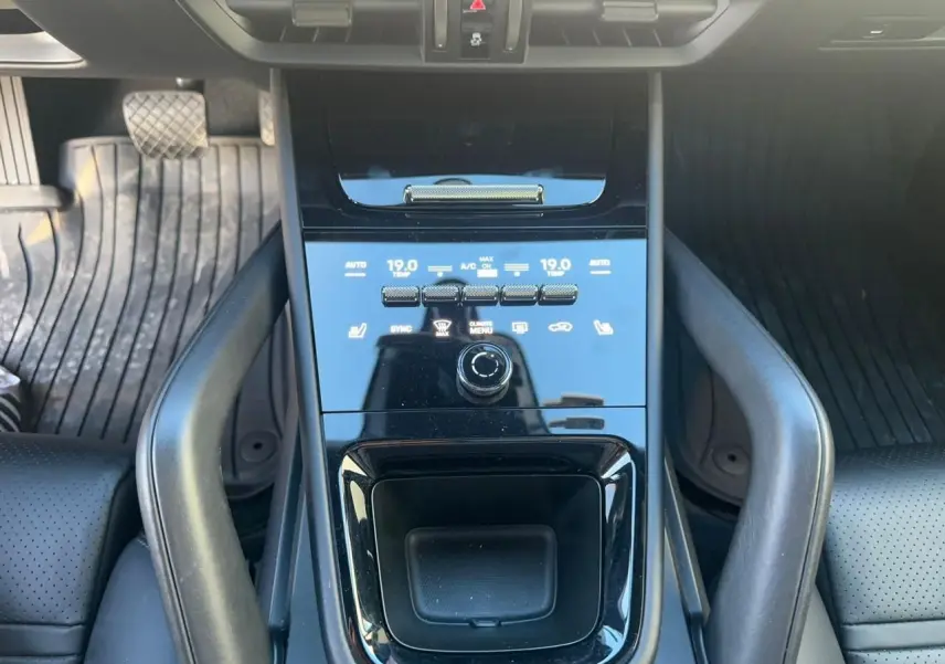 Vue rapprochée de la console centrale noire brillante du Porsche Cayenne 2024 avec commandes climatisation et espace de rangement.