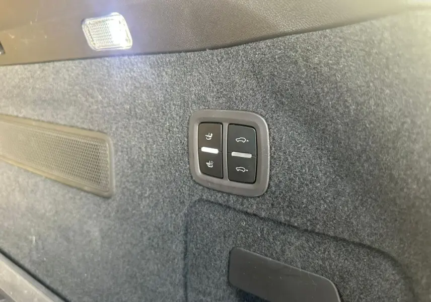 Boutons de réglage des sièges et ouverture du coffre sur la garniture intérieure grise du coffre d’un Porsche Cayenne 2024.