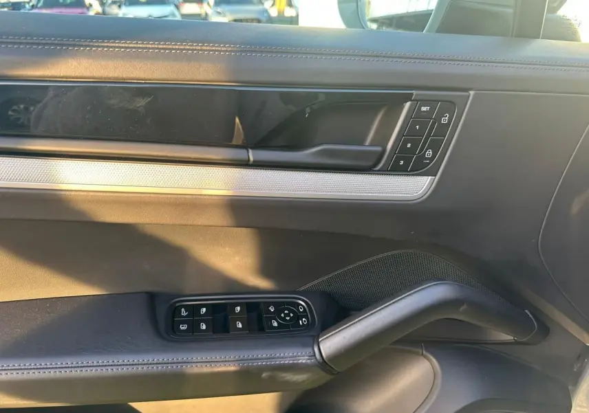 Vue intérieure côté gauche de la porte d’une Porsche Cayenne 2024 gris arctique, avec commandes de vitres et verrouillage.