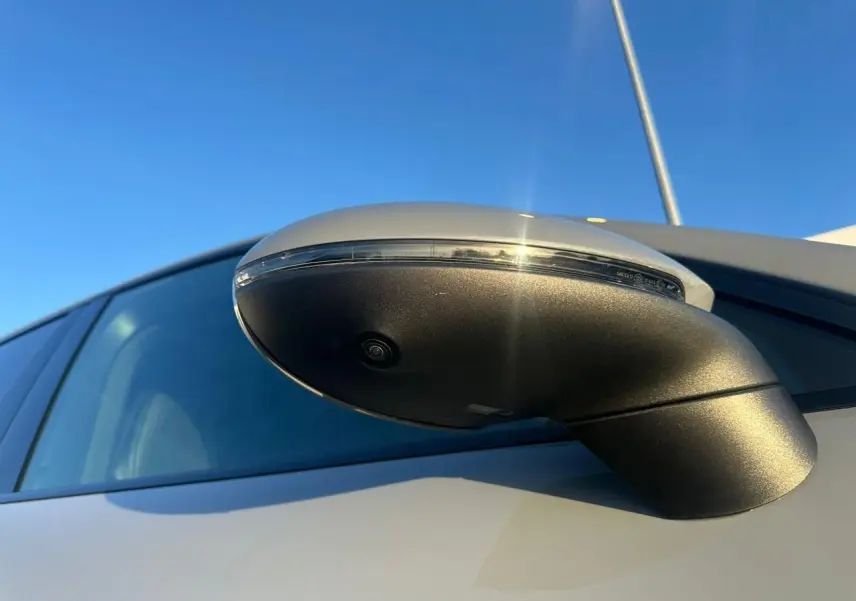 Gros plan sur le rétroviseur côté droit gris arctique du Porsche Cayenne III Coupe 2024, avec caméra intégrée visible.