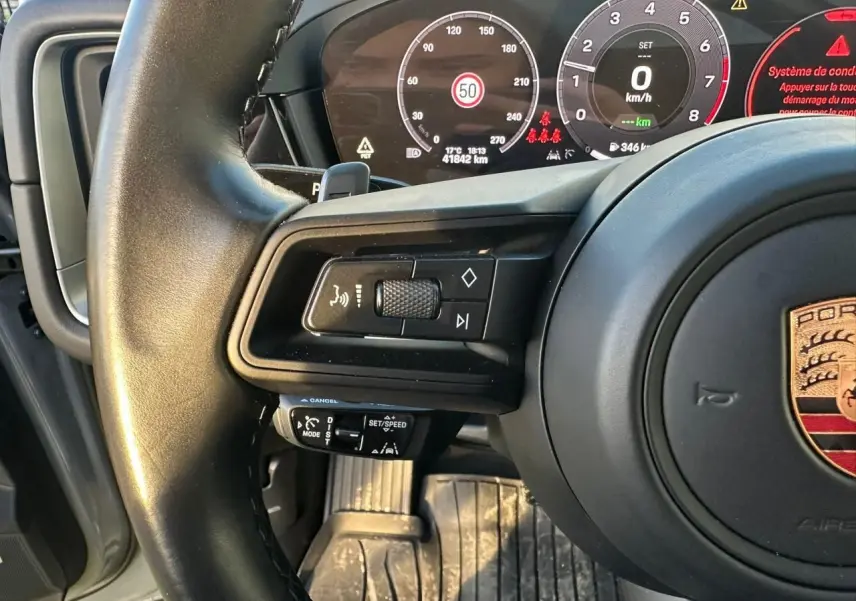 Gros plan sur le volant et le tableau de bord numérique du Porsche Cayenne 2024, avec commandes au volant visibles.