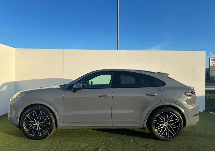Vue de profil côté gauche d'un Porsche Cayenne Coupé 2024 en gris arctique avec jantes noires à rayons fins.