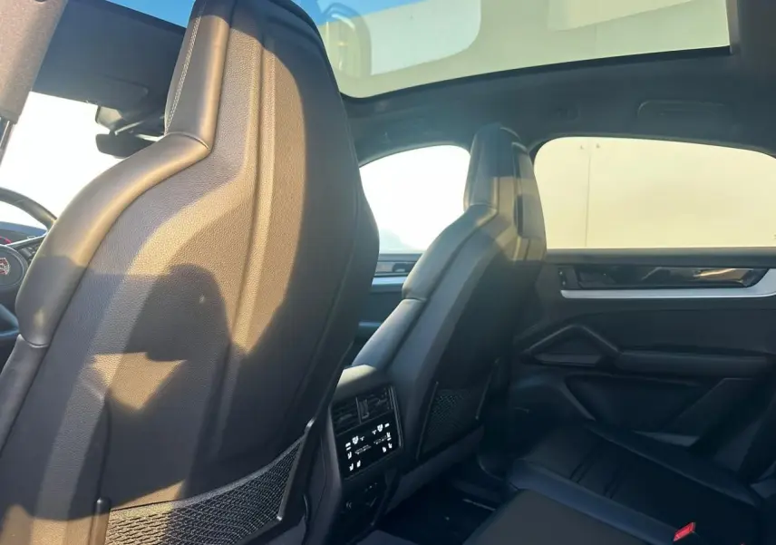 Vue intérieure arrière du Porsche Cayenne 2024 gris arctique, montrant les sièges avant en cuir noir et toit panoramique.