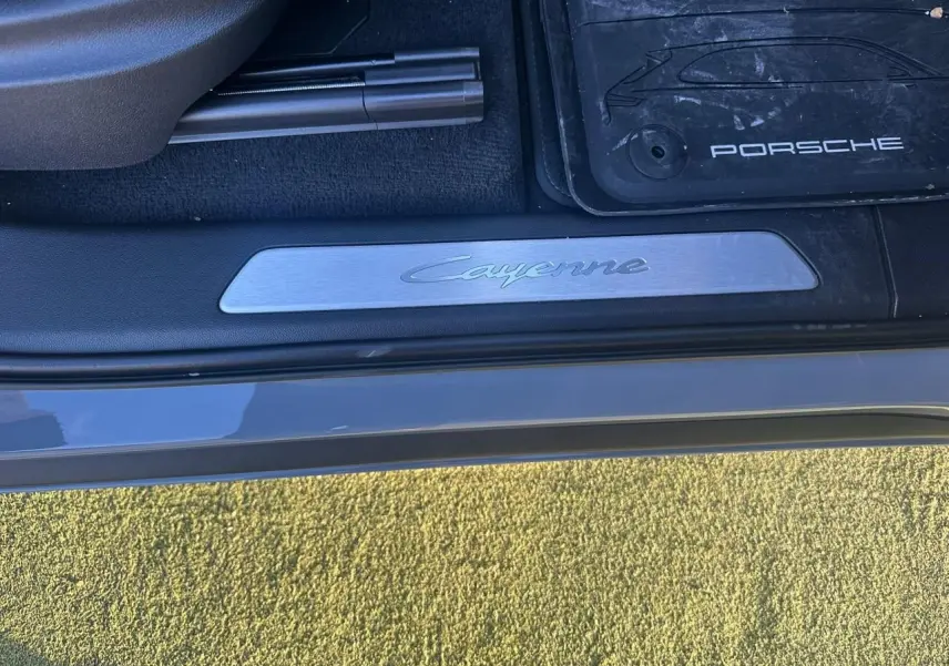 Gros plan sur la plaque de seuil de porte côté conducteur du Porsche Cayenne gris arctique avec tapis de sol Porsche visible.
