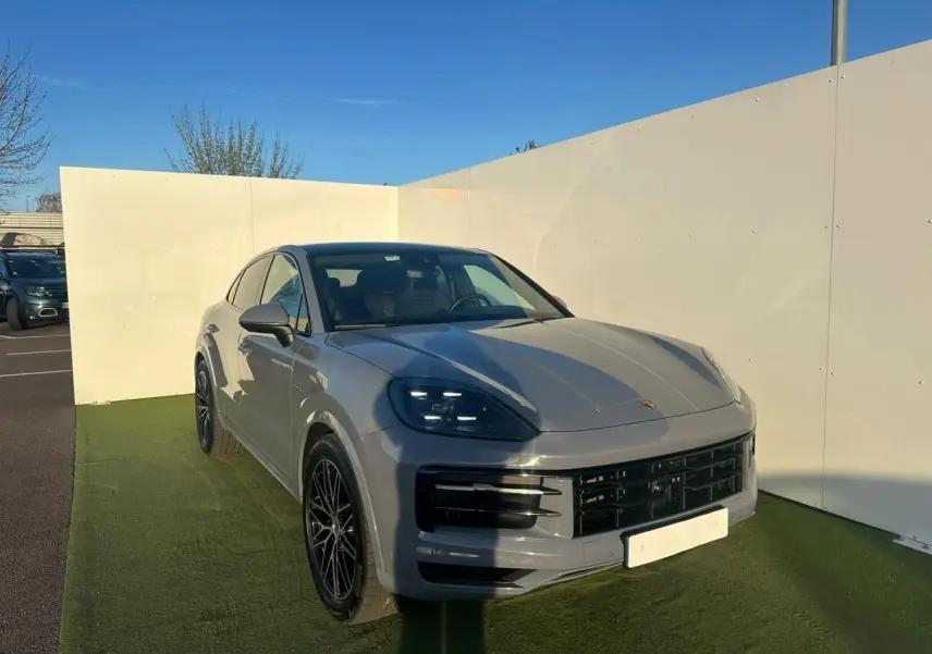 Vue 3/4 avant droite du Porsche Cayenne III Coupe 3.0 V6 S E-Hybrid 2024 en gris arctique avec jantes noires.
