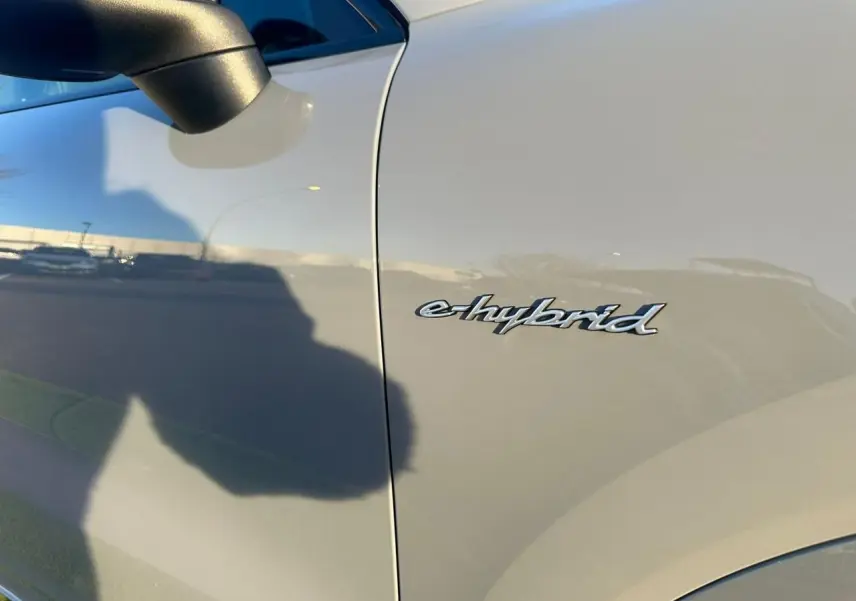 Gros plan sur l’inscription e-hybrid côté gauche d’un Porsche Cayenne Coupé gris arctique 2024, avec rétroviseur noir.