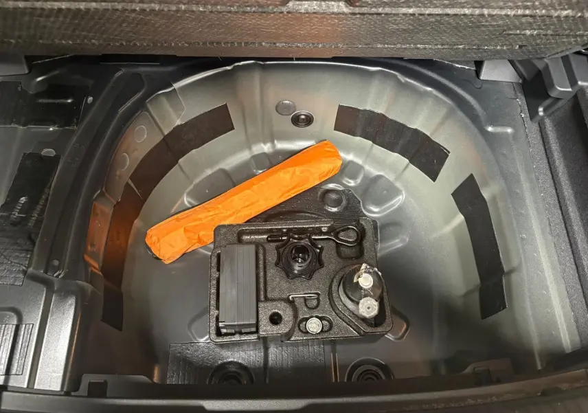 Vue plongeante sur le coffre ouvert de la Volkswagen Polo noir intense, montrant le rangement sous plancher avec kit de dépannage.