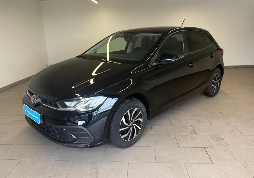 Volkswagen Polo noir intense vue 3/4 avant droit, jantes alliage et calandre chromée visible en intérieur showroom.