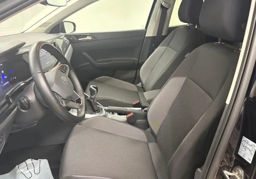 Vue intérieure côté conducteur de la Volkswagen Polo 2025, sièges tissu gris et volant cuir avec levier de vitesses manuel.