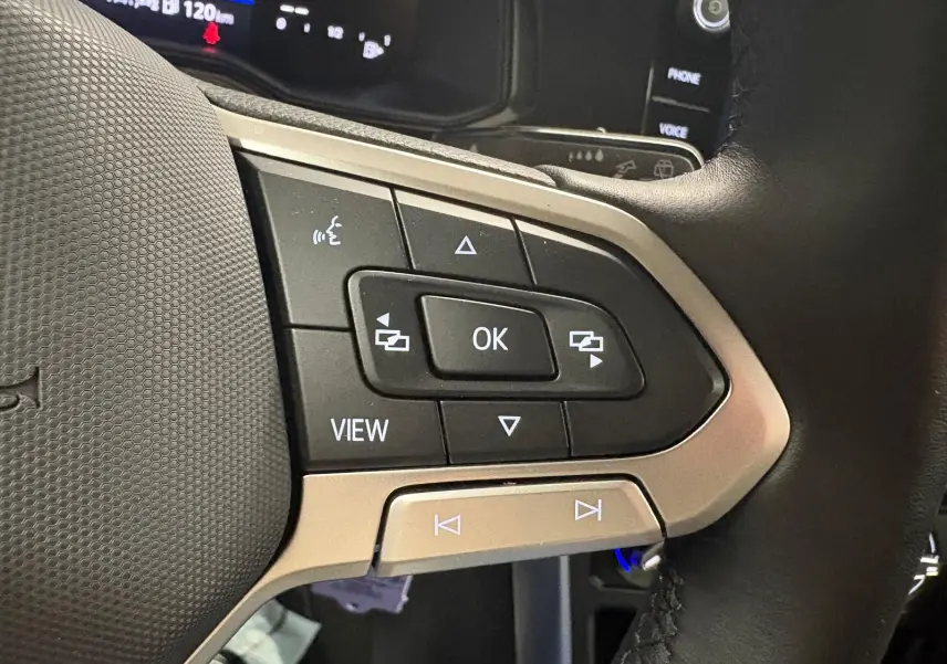 Gros plan sur les commandes multifonctions du volant cuir d'une Volkswagen Polo noire intense, avec écran digital en arrière-plan.