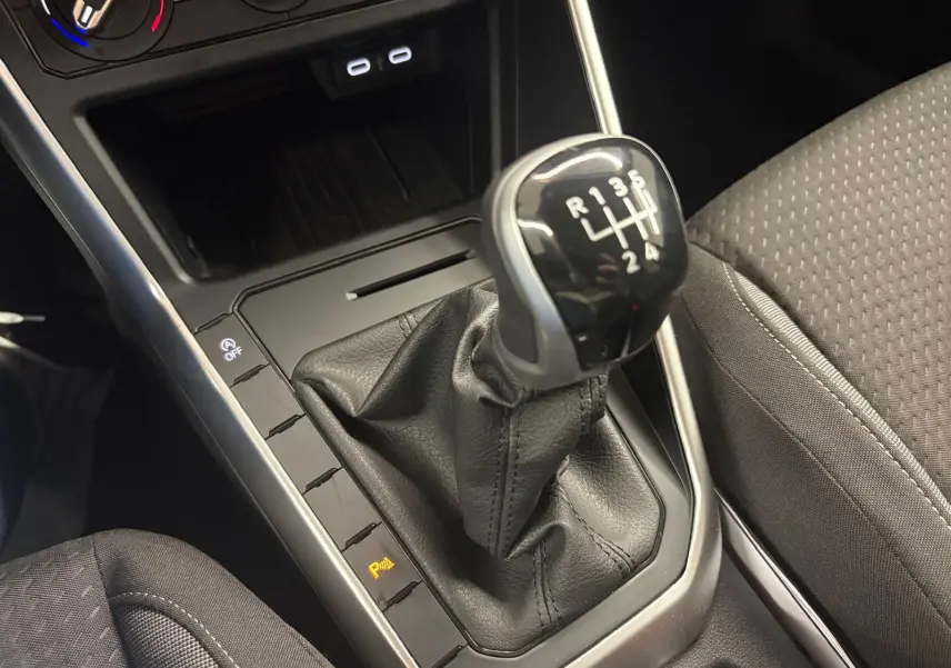 Gros plan sur levier de vitesses manuel noir et console centrale avec sièges tissu gris dans Volkswagen Polo 2025.