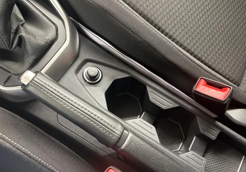 Gros plan intérieur sur le frein à main en cuir, prise 12V et porte-gobelets entre les sièges avant noirs.