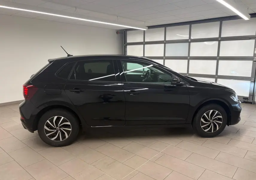 Vue de profil côté gauche d'une Volkswagen Polo noire intense 2025 avec jantes alliage 15 pouces dans un garage.