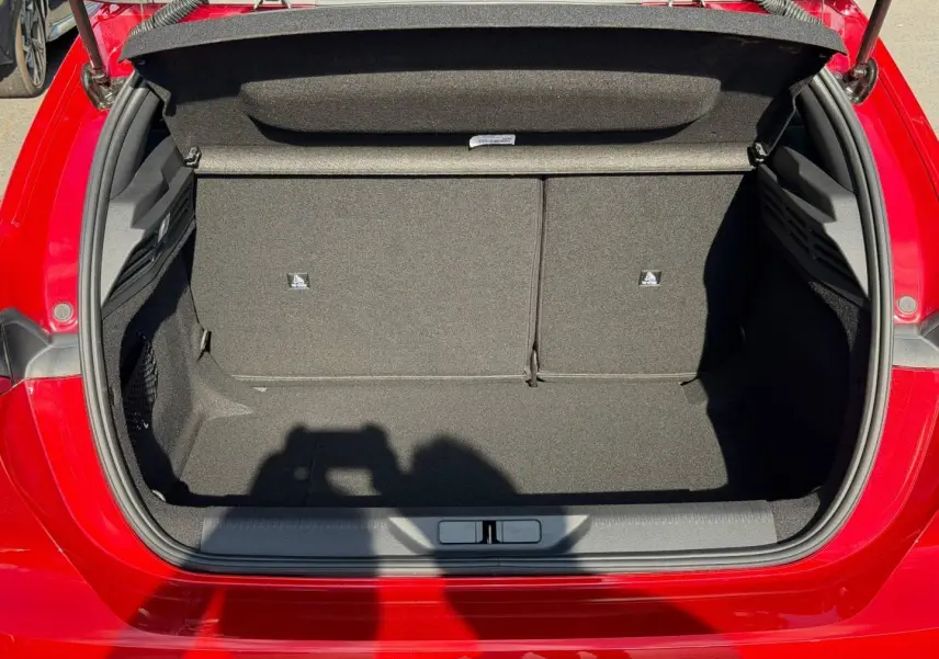 Coffre ouvert vu de l'arrière d'une Peugeot 308 rouge Elixir, montrant un espace de rangement propre et vide.