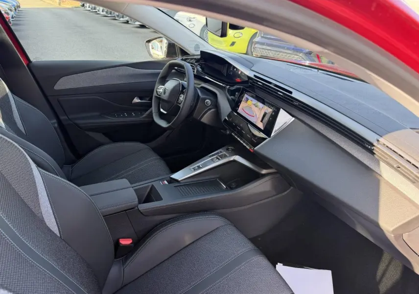 Intérieur côté conducteur de la Peugeot 308 rouge Elixir, avec tableau de bord moderne et écran tactile affichant la caméra de recul.