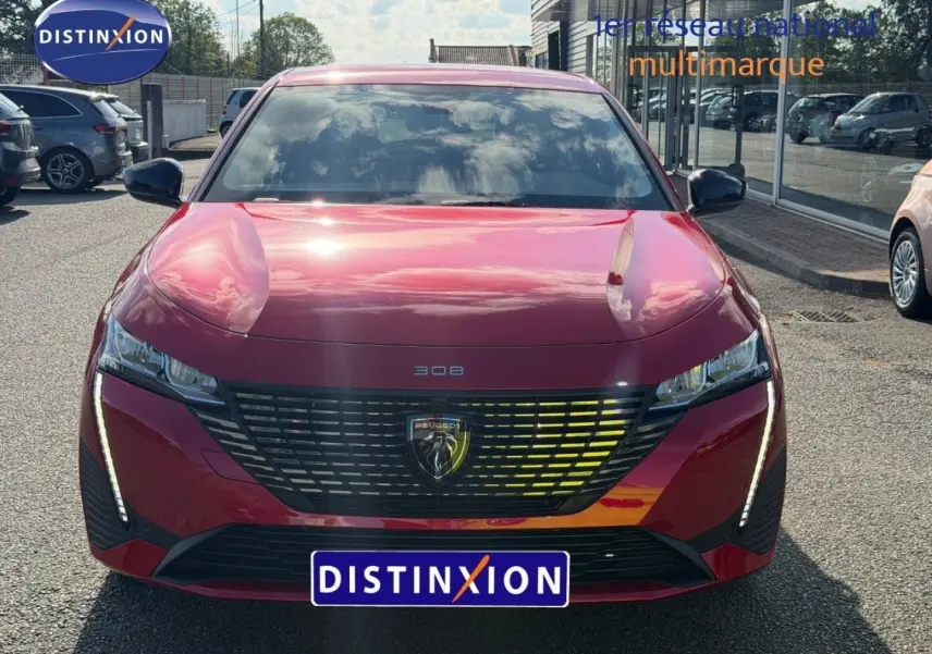 Vue frontale d'une Peugeot 308 rouge Elixir 2025 avec calandre noire et feux LED verticaux allumés.