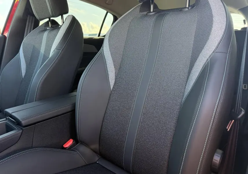 Gros plan sur les sièges avant en tissu et cuir noir avec surpiqûres blanches dans l'habitacle d'une Peugeot 308 rouge.