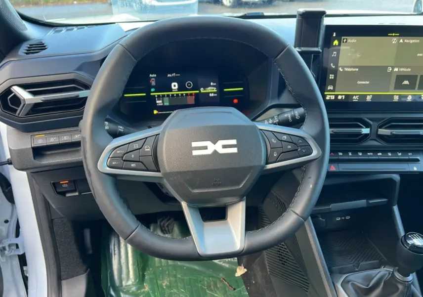 Vue intérieure centrée sur le volant multifonction et le tableau de bord numérique du Dacia Duster blanc glacier 2025.