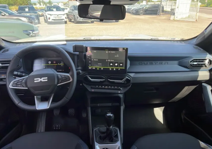 Intérieur du Dacia Duster 2025 blanc glacier, vue frontale sur le tableau de bord avec écran tactile et volant multifonction.