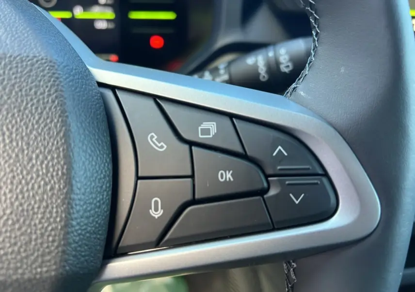 Gros plan sur les commandes multifonctions à droite du volant du Dacia Duster blanc glacier 2025, version Journey Plus.