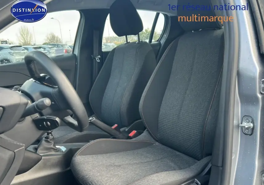 Vue intérieure côté conducteur de la Peugeot 208 gris artense, montrant les sièges et la boîte manuelle.