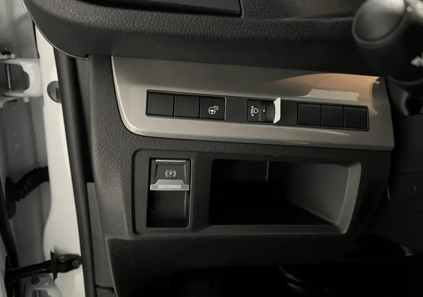 Détail de la console côté gauche du tableau de bord du Peugeot Expert Fourgon blanc 2024 avec commandes du frein de stationnement et réglage des phares.