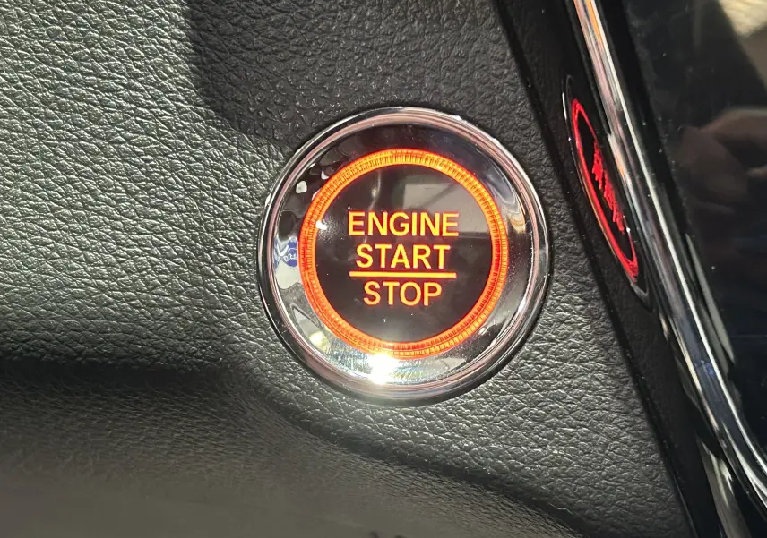 Gros plan sur le bouton start/stop moteur éclairé en orange dans l'habitacle noir du Honda HR-V 2020.