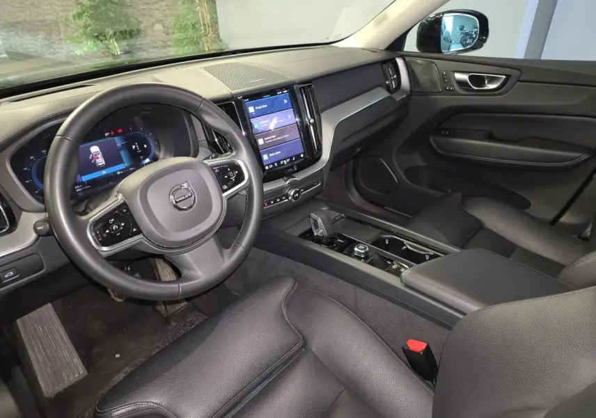 Vue intérieure côté conducteur du Volvo XC60 noir, avec tableau de bord digital et écran tactile central vertical.